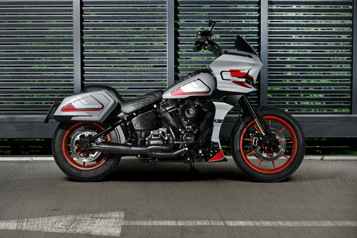 A silver and black FXLRST Low Rider ST motorcycle with red accents, parked in profile against a dark gray slatted metal wall.