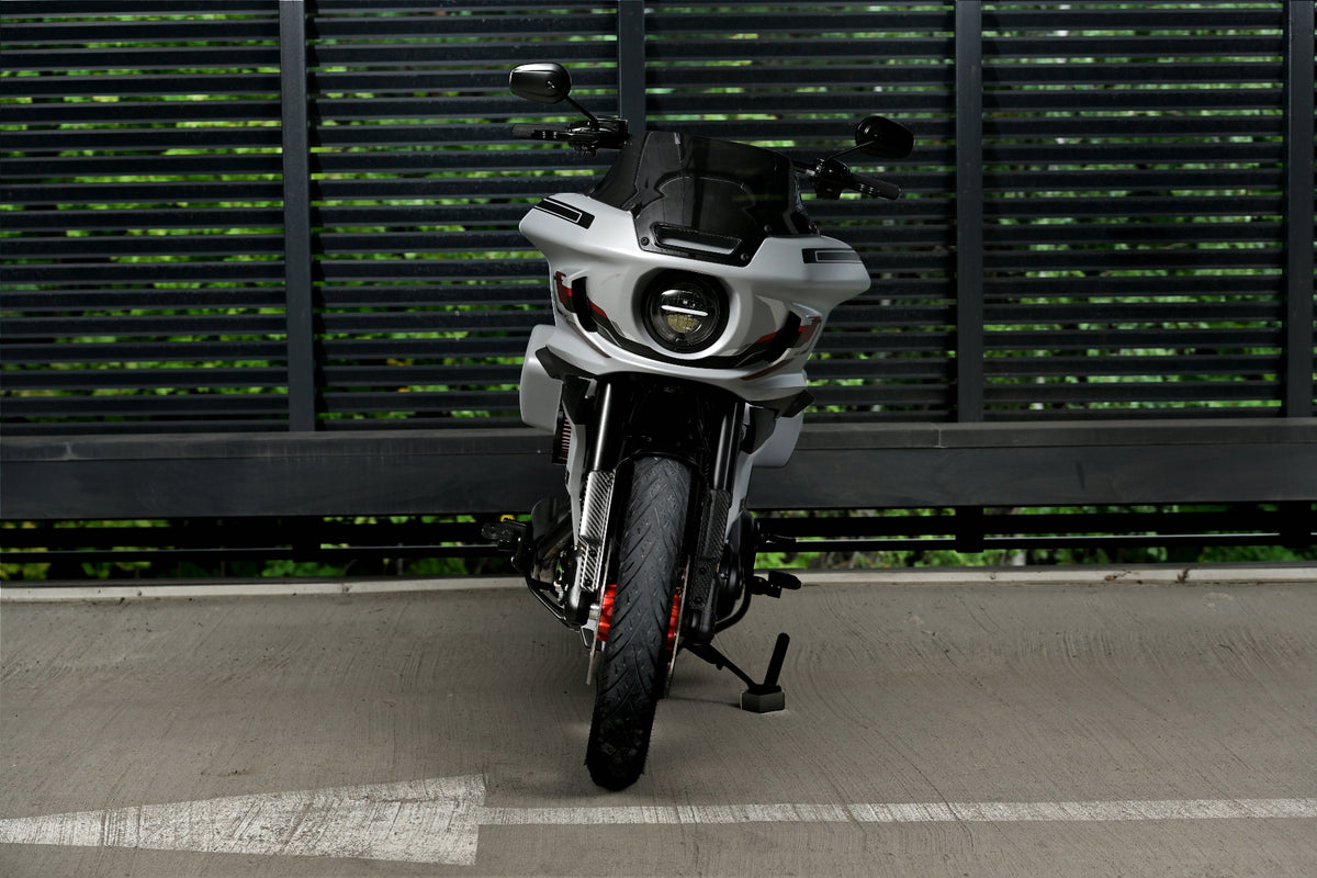 A white and black dual-sport motorcycle with red accents, parked on a concrete surface in front of a dark green slatted metal fence.