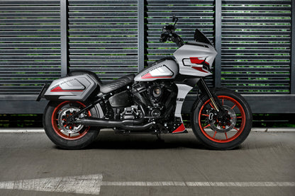 A silver and black FXLRST Low Rider ST motorcycle with red accents, parked in profile against a dark gray slatted metal wall.