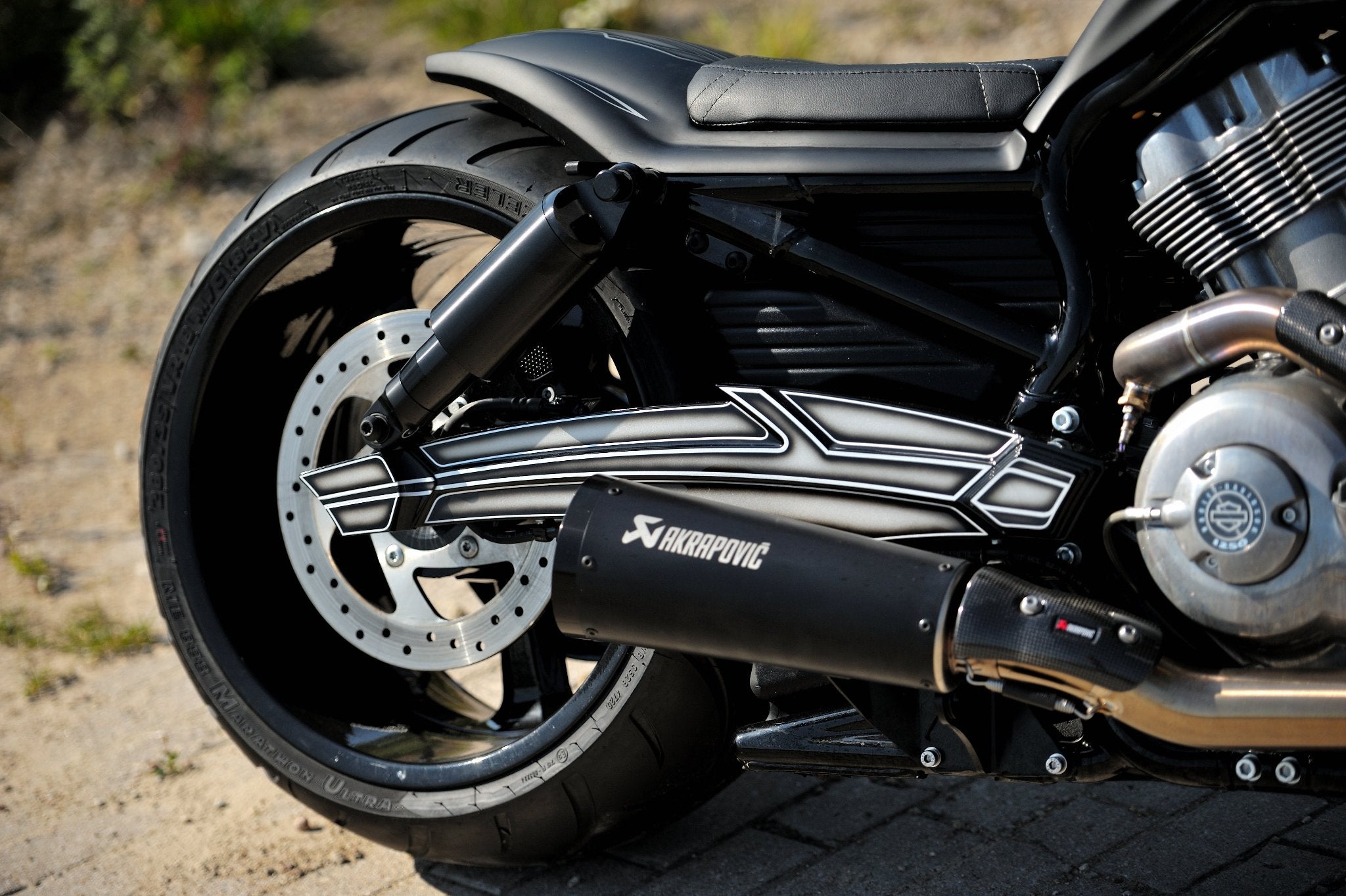 Custom CNC machined rear fork for Harley Davidson V-Rod models mounted on a V-Rod Muscle. Next to there is an Akrapovic exhaust visible.